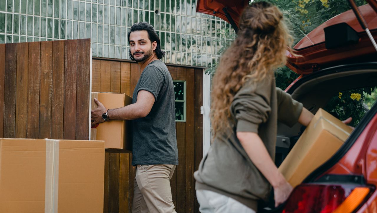 Pareja descargando cajas de mudanza en el jardín de su nueva casa
